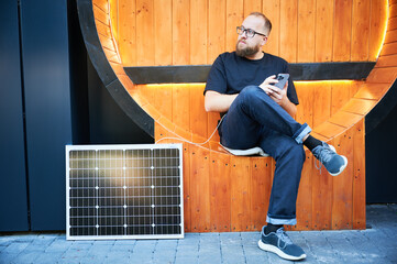 Bearded man using smartphone connected to photovoltaic solar panel. Integration of sustainable...