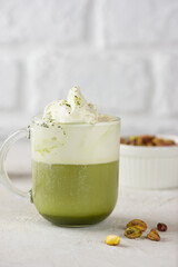 Green matcha tea mixed with milk and pistachio in latte glass on table. Vertical orientation.