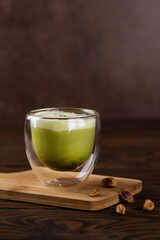 Pistachio matcha latte tea with whipped milk in a glass on a wooden board. Vertical orientation.
