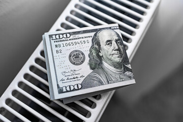 A stack of hundred-dollar bills lies on a white radiator, symbolizing wealth, savings, and...