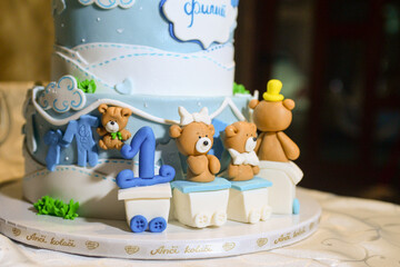 A three-tier blue and white birthday cake decorated with fondant, figurines in the shape of bears and a bunny with the male name Philip written in Cyrillic.