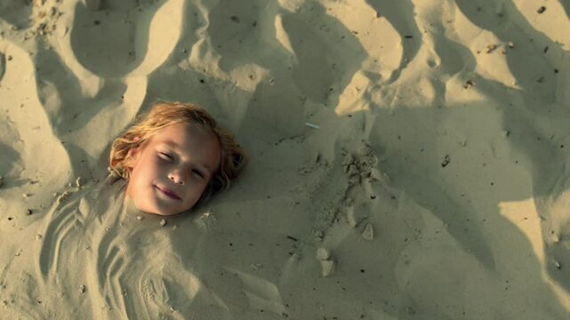 small girl buried in sand of beach