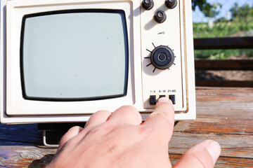 A hand interacts with a vintage television, pressing control buttons. This shot emphasizes...