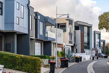 Row of modern multi-storey townhouses in a contemporary Australian suburb. Wheelie rubbish bins are...
