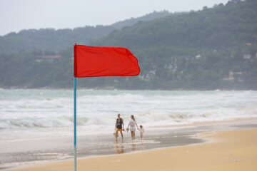 Red warning flag on background of a sea beach on walking people background. Sign indicating that swimming is prohibited during storm