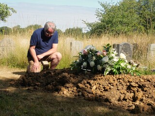 Elderly Man Grieving at a fresh Graveside on a warm day