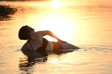 photo shoot of a woman in a white pareo and a black swimsuit at sunset on the beach
