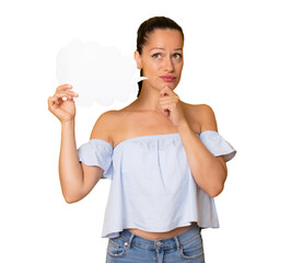 Portrait of beautiful doubtful young woman holding blank paper speech cloud in hand and holding...