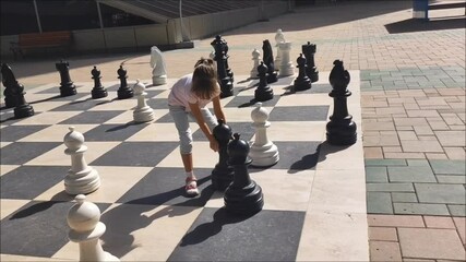 little girl is playing with gigant chess outdoor