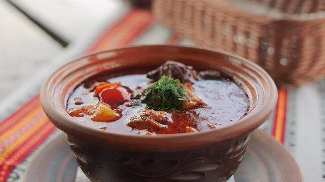 Traditional Hungarian bograch soup with meat, vegetables, and spices served in clay pot, authentic hearty dish from Zakarpattia region on ethnic tablecloth in rustic setting