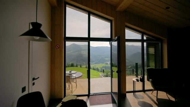 Modern wooden house interior with large glass doors opened to panoramic Carpathian mountain view, peaceful vacation retreat with natural light and scenic landscape outside