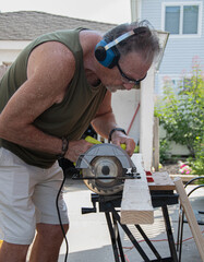 Senior citizen doing carpentry work with a circular saw.