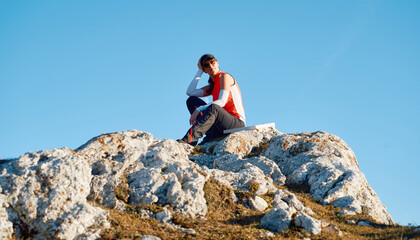 Obraz premium A female hiker enjoys the serene beauty of the mountain landscape, sitting on a rock at the summit, surrounded by breathtaking scenery and a sense of tranquility.