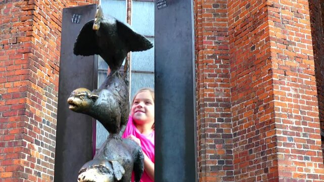 Little beautiful girl walks near the monument to Bremen Town Musicians located near the Church of the Holy Spirit in Riga, Latvia.