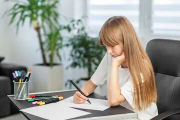 Focused girl drawing on paper at desk. Back to school.