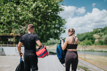 A man and a woman dressed in athletic wear walking near greenery carrying sporting equipment on a sunny day. The picture radiates themes of sport, health, and outdoor activity.