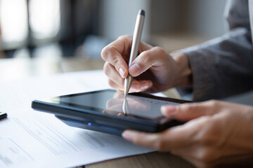 A hand signs a digital document on a tablet with a pen, symbolizing electronic signatures and modern business agreements