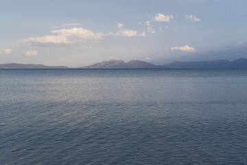 A serene seascape stretching toward distant mountains. The sea surface has gentle ripples and the...