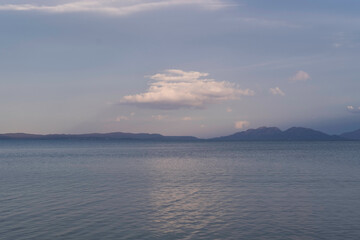 A serene seascape stretching toward distant mountains. The sea surface has gentle ripples and the...