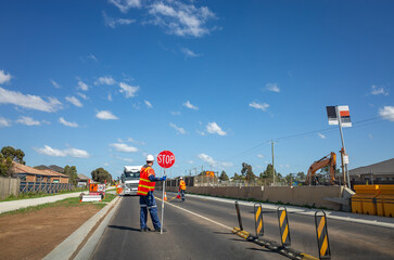 Traffic control personnel managing vehicle flow with a stop and slow sign at a suburban road...