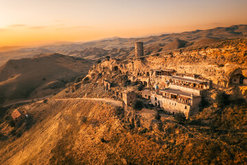 Aerial view of an ancient Orthodox monastery carved into remote cliffs amid vast hills, symbolizing...