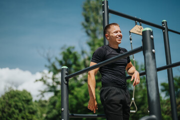 A man is smiling during an outdoor fitness training session in a park under blue skies. The weather...