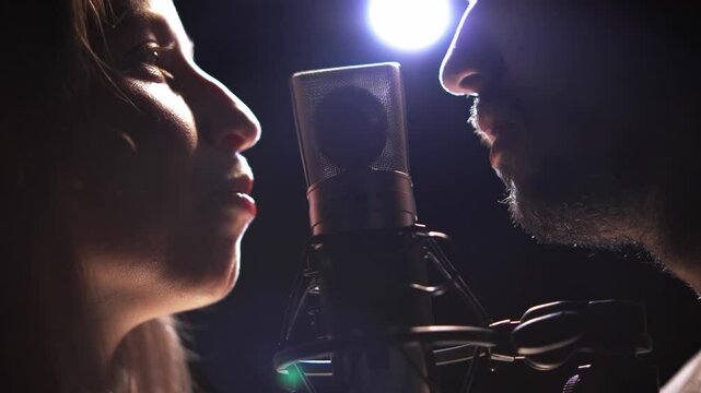 Man and woman recording voices on microphone in dubbing studio