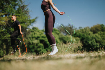 A sporty couple engaging in jump rope workouts in a lush park during a sunny day.