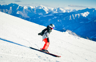 Young skier wearing helmet skiing downhill on snowy mountain, dynamic outdoor winter sports action