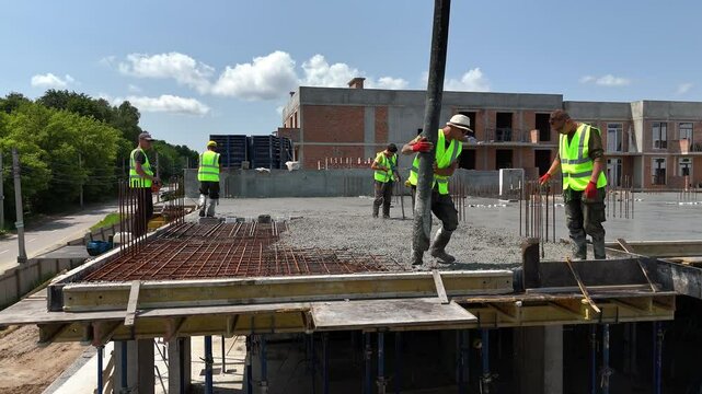 Construction workers in safety vests pouring concrete on top floor slab of building site, teamwork and manual labor in civil engineering and modern residential development