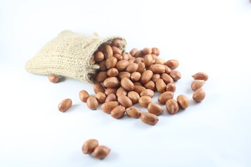 A rustic burlap sack overflows with peanuts onto a clean white surface, highlighting natural,...