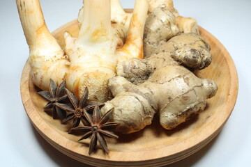 Fresh galangal, ginger, and dried star anise on a wooden plate. Natural herbal spices used in Asian cooking and traditional remedies