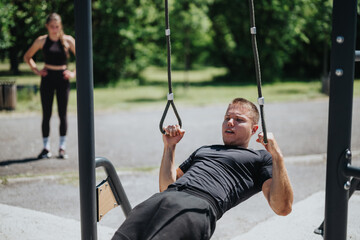 A man trains using resistance bands outdoors, focusing on strength. A woman observes nearby,...