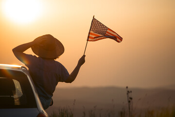 Woman in the car holding a waving american USA flag in the sunset