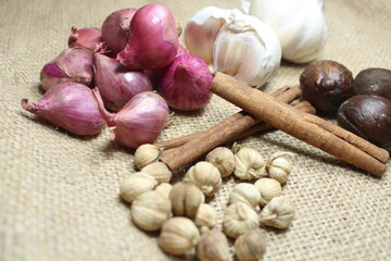 Spices vibrant mix of shallots, garlic, nutmeg, cinnamon sticks, and cardamom pods arranged on...