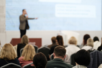 Conference presentation featuring speaker on stage and audience members paying attention,...