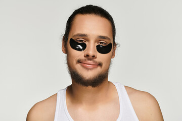 Handsome young bearded man enjoying self care routine with eye patches