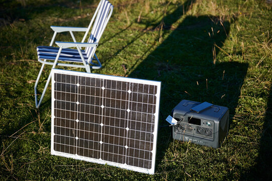 Close-up of solar panel connected to portable power station on grassy field.
