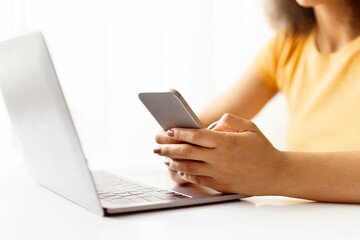 Closeup of female hands holding smartphone in front of laptop. Remote communication, online...