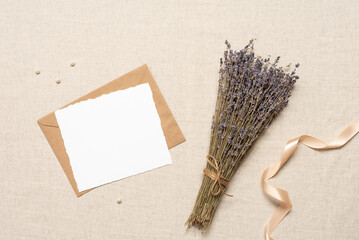 Blank white card mockup, brown envelope and dried lavender bouquet on beige linen fabric, wedding...