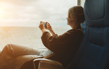 Woman taking photo of sea through ferry window.