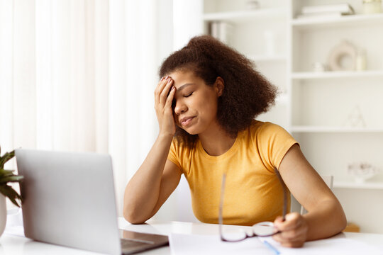 Frustrated young black woman with hand on face and holding glasses. Feeling tired or disappointed during online work or remote study from home desk, closeup