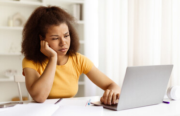 Frustrated young black woman looking at laptop with hand on face, feeling stressed or overwhelmed...