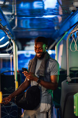 Smiling sportsman using smartphone and listening music on bus after training