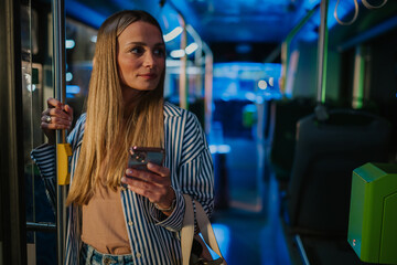 Young woman using smartphone while standing on a bus at night