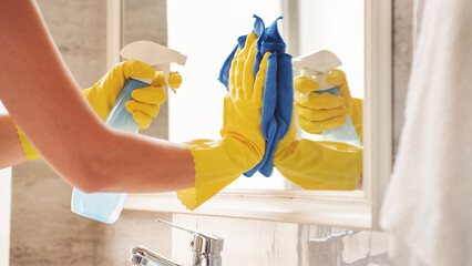 Woman cleaning mirror in bathroom 