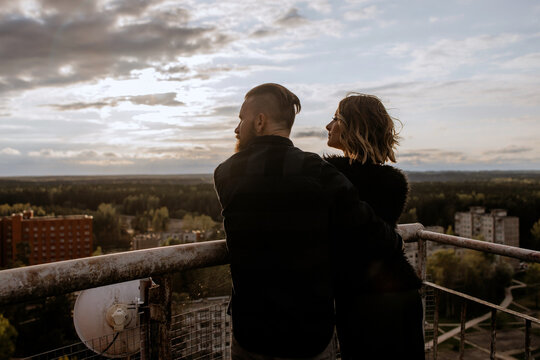 Romantic Couple Embracing on Rooftop Balcony at Sunset — Rear View Overlooking Scenic Cityscape and Forest Horizon