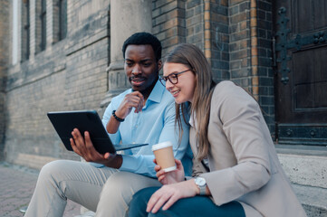 Business colleagues using tablet and drinking coffee outdoors