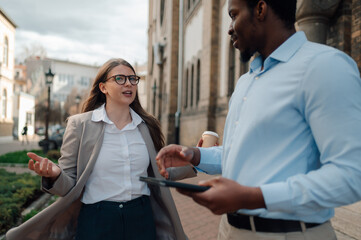 Business colleagues discussing work while walking and holding digital tablet and coffee