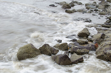Waves crashing over the beach rocks, rocks and ocean with blurred motion of waves, rocky shoreline meeting coastal waters